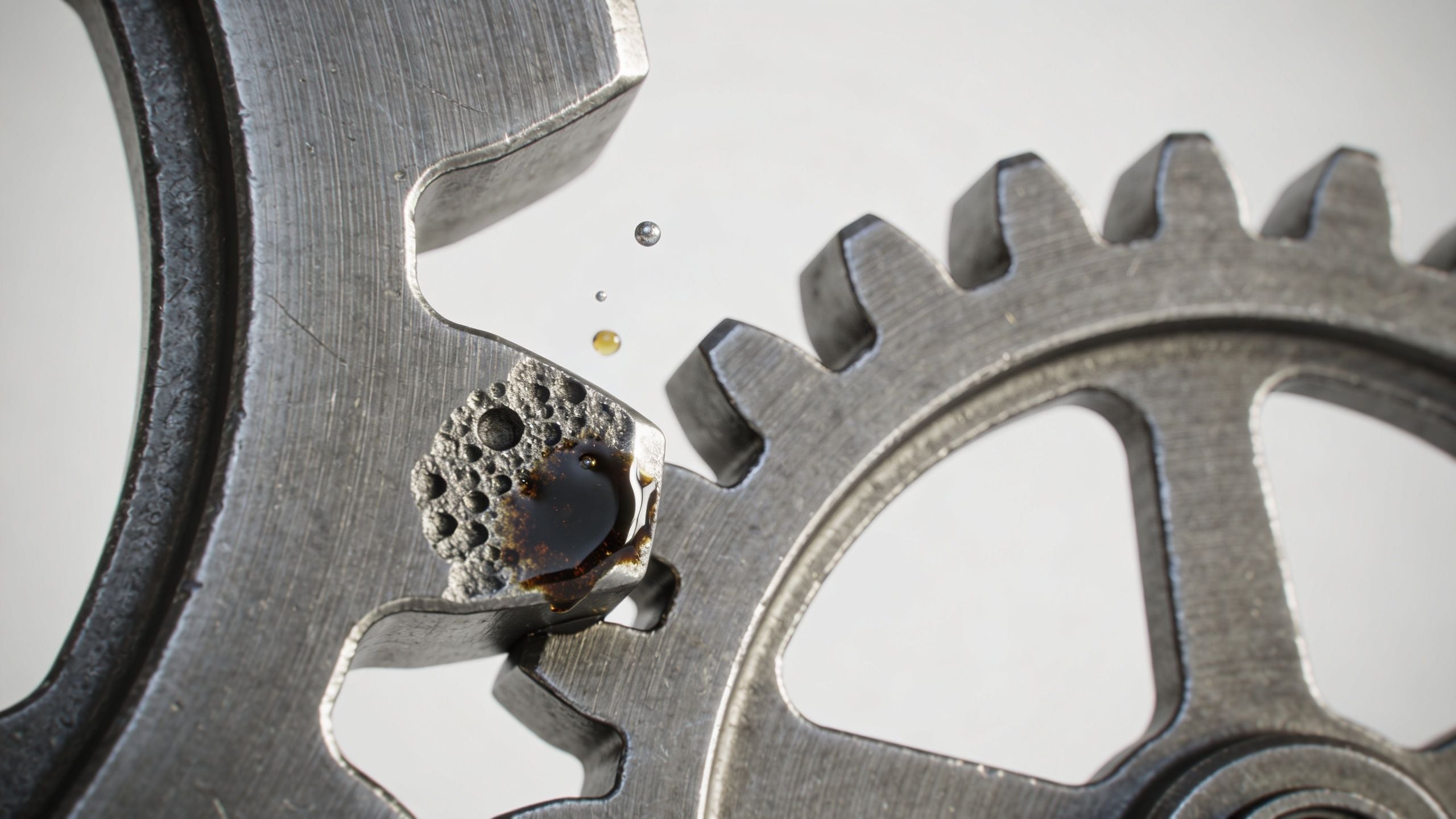 Macro view of metal gear teeth with lubricant oil and air bubbles indicating mechanical wear and damage.